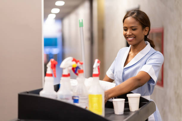 Beautiful black cleaner working at hotel pushing cart with cleaning supplies smiling very happy